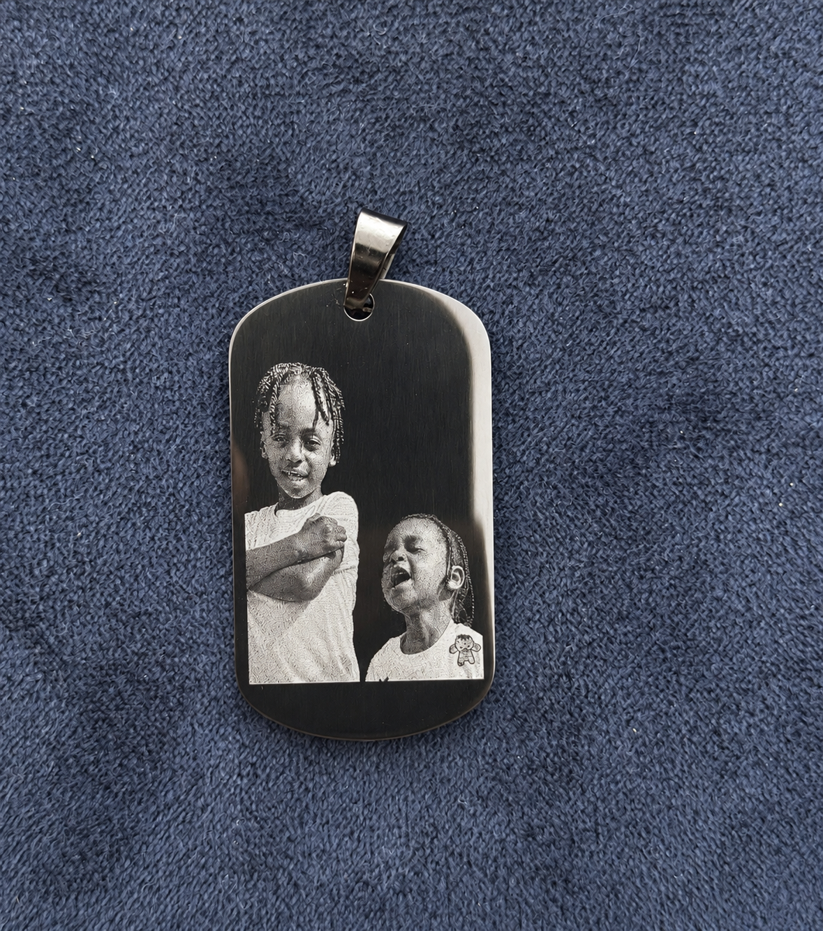 Two children’s portraits engraved on a black metal dog tag